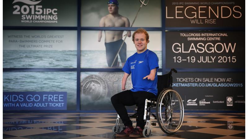 Man in wheelchair poses in front of a wallpaper