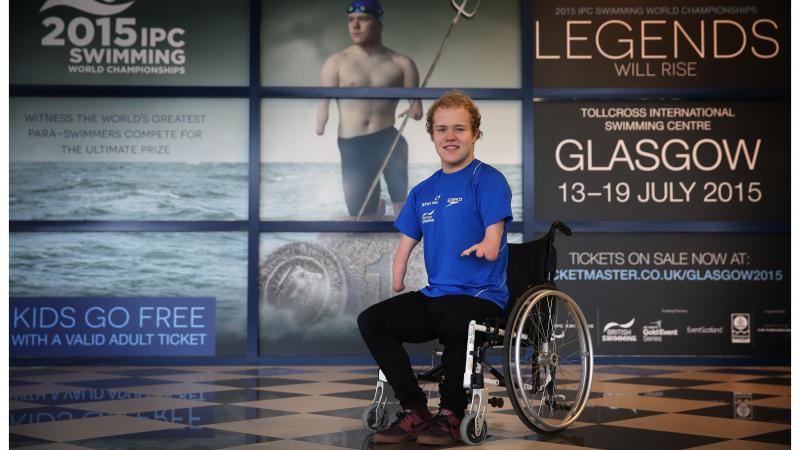 Man in wheelchair poses in front of a wallpaper