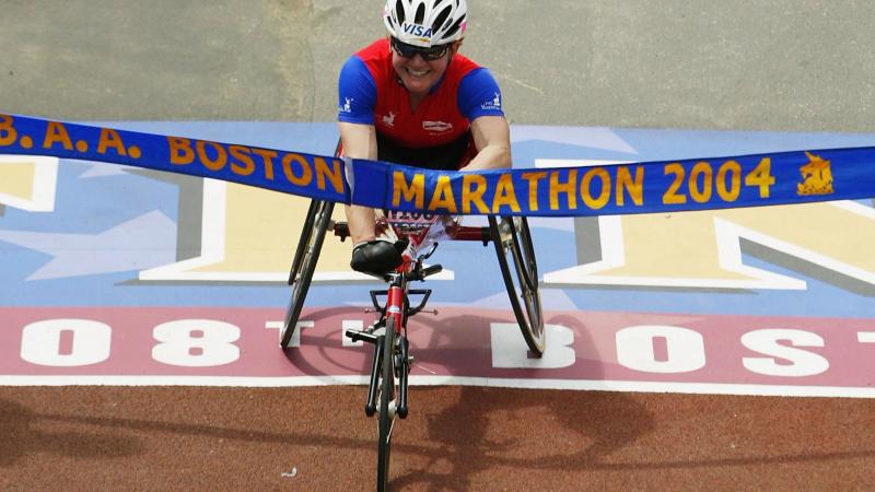 Women in racing wheelchair crosses a finish line