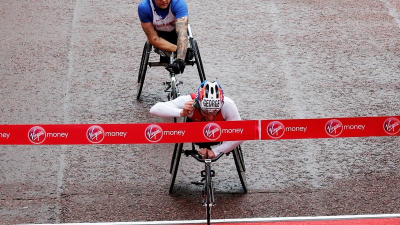 A wheelchair racer cuts through the finishing tape on a wet damp road.