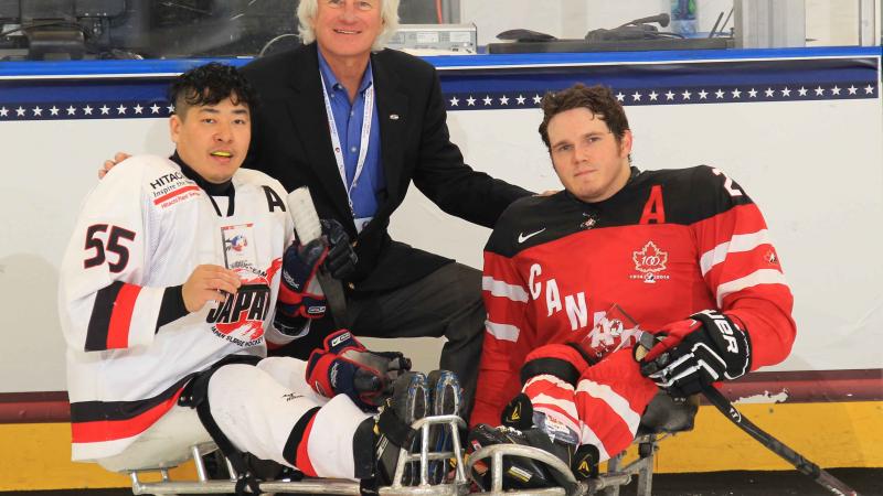 Two sledge hockey players and a man in a suit posing for the camera