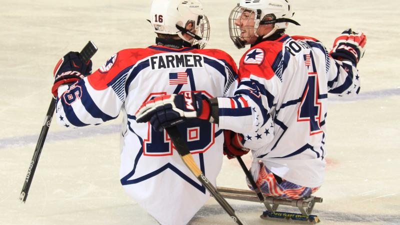 Two sledge hockey players on the ice, in a conversation