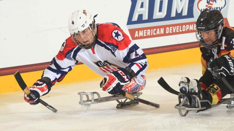 Two sledge hockey players chasing after the puck.