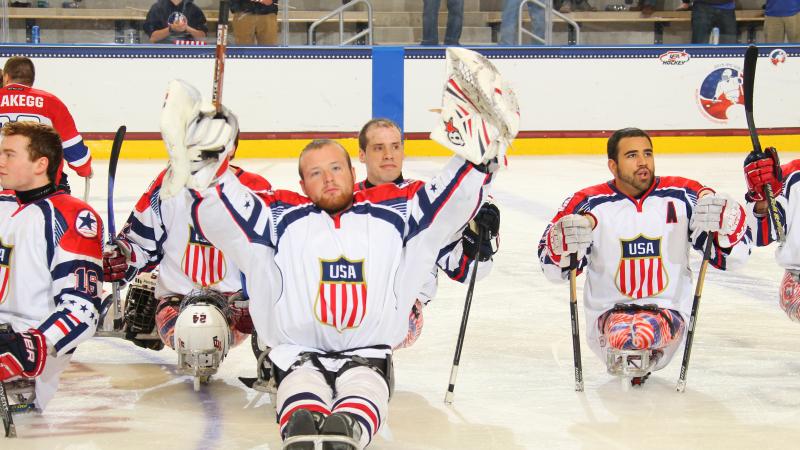 Sledge hockey players on the ice without their helmets, celebrating