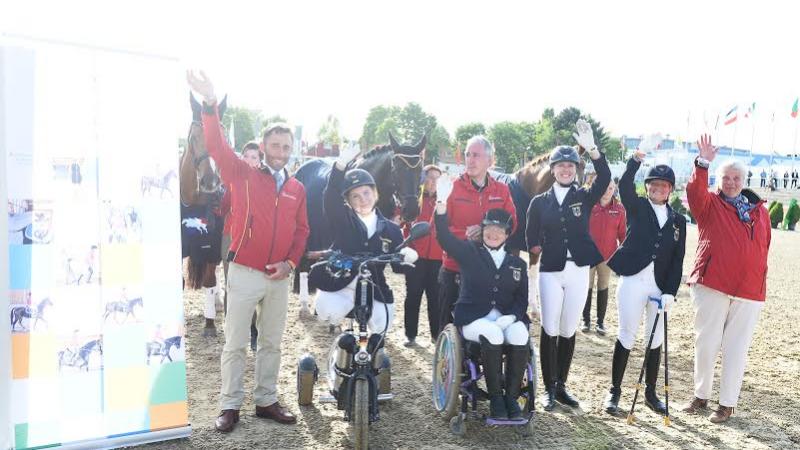 Group shot of seven people and horses in the background, waving to the camera