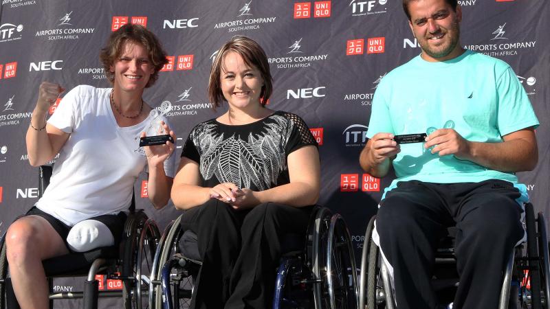 Three people in wheelchairs posing in front of a branded backdrop