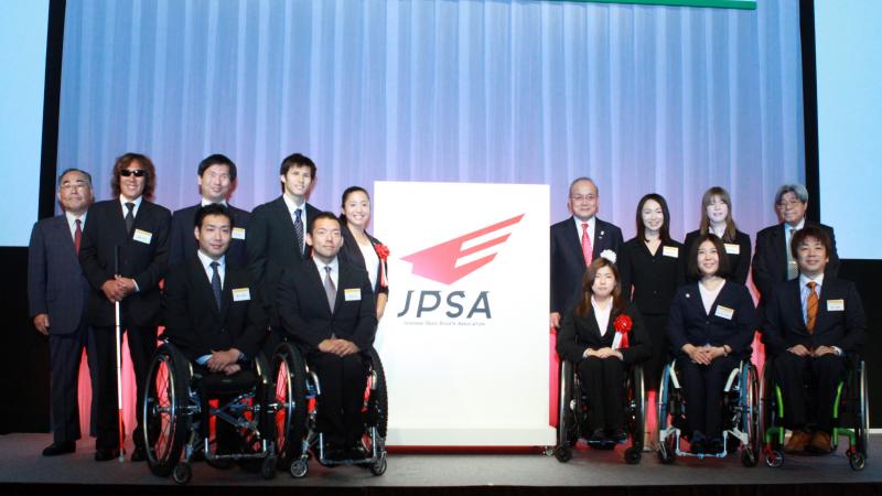 Group shot of around 20 people standing and in wheelchairs with a big banner