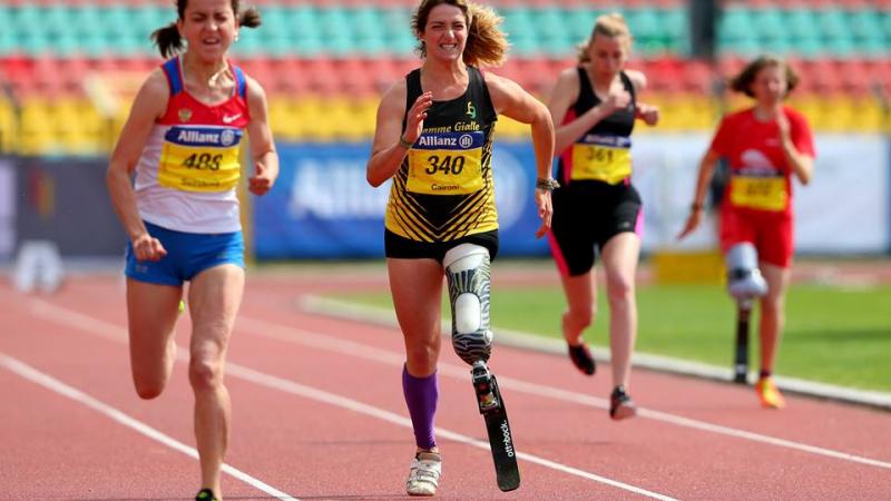 A woman with a running blade clenches her face in effort as she sprints forward.