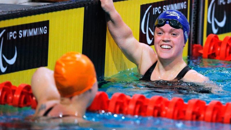 Two women smiling at each other in a swimmig pool after a race