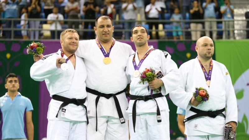 Four male judoka pose on podium