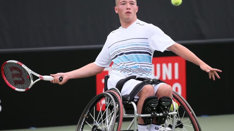 Wheelchair tennis player hits a ball back.