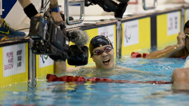 Man in swimming pool, celebrating after finishing a race. Camera filming him.