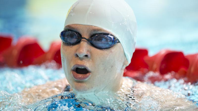 Portrait picture of a swimmer with a white swim cap and swim goggles.