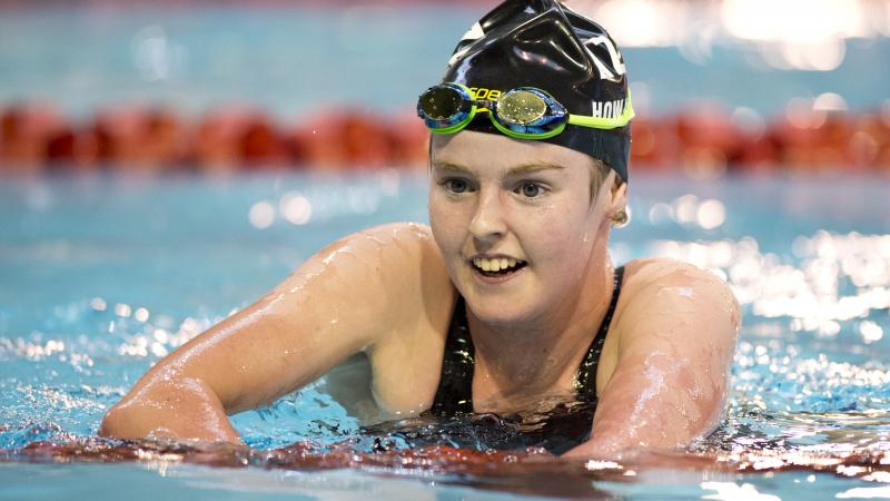 Woman in swimming pool, upper body is out of the water, smiling