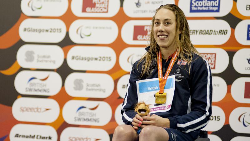 Woman in a wheelchair, on a podium with medal around her neck