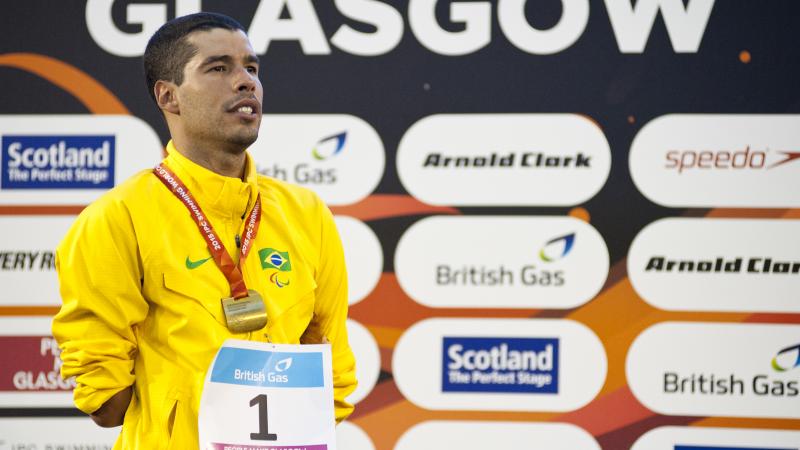 Man in yellow jacket standing ona podium, wearing a gold medal