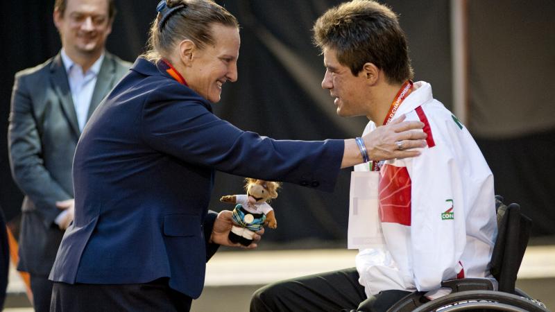 Man in wheelchair on the podium receiving a medal from a woman