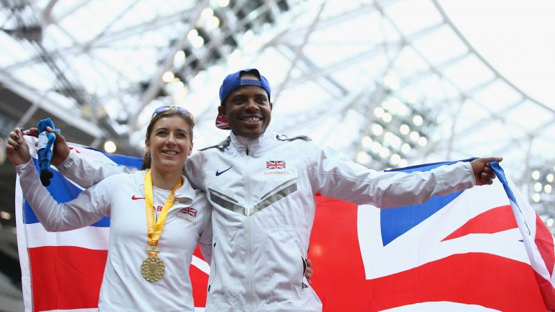 Man and woman on podium with a medal around her neck and a British flag