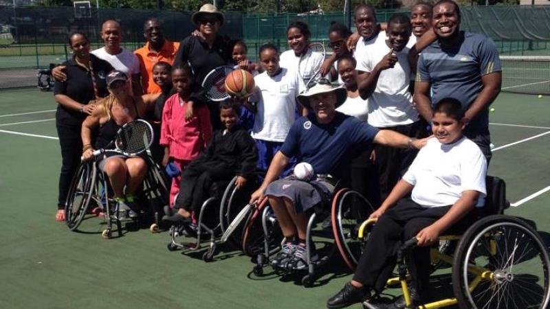 Group picture of people in wheelchairs and standing on a tennis court