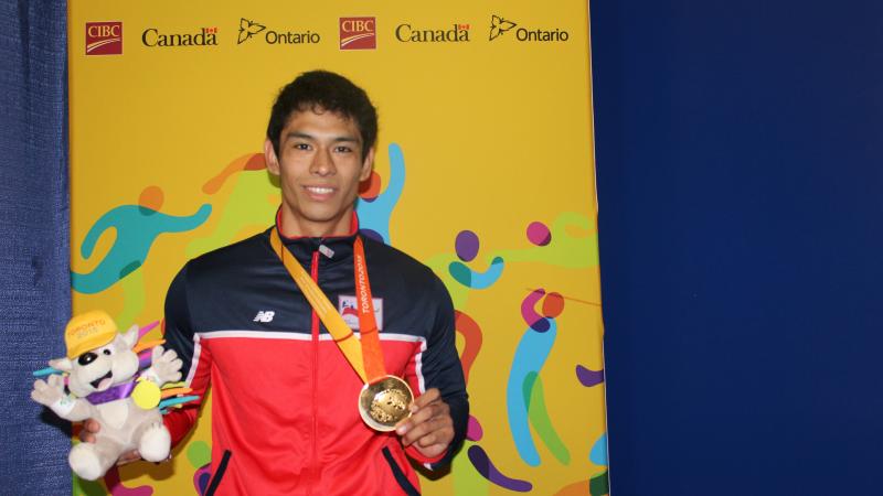 Jorge Carinao Cárdenas claims gold on the first day of powerlifting at the Toronto 2015 Parapan American Games on Saturday (8 August). He faces the camera holding the TO2015 mascot and his gold medal.
