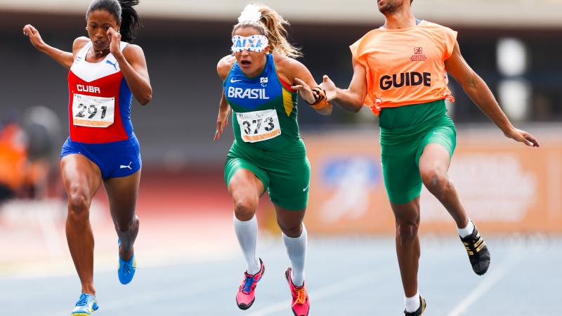 blindfolded runner with guide and another female runner crossing a finish line