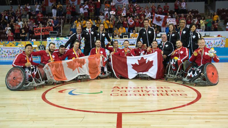 Team photo of a celebrating group of men sitting in wheelchairs, showing Canadian flags