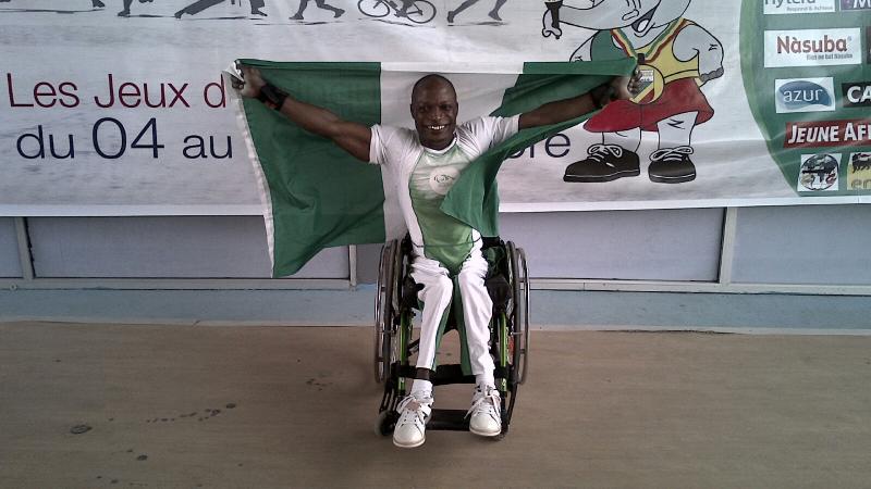 Man in a wheelchair, holding a Nigerian flag and celebrating