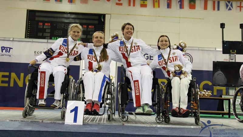 Four women in wheelchairs on a podium, posing with medals 