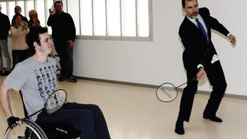 Two men, one standing, one in a wheelchair playing badminton