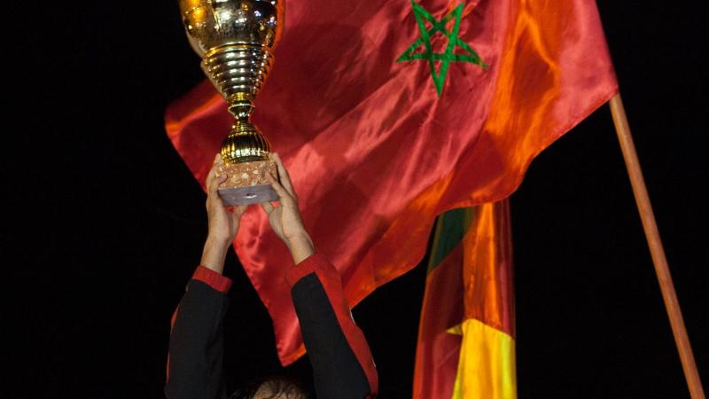 Man celebrates victory by raising football cup.