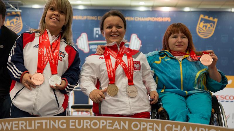 Three women with medals around their necks posing on the podium