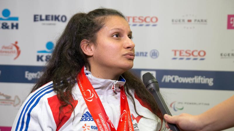 Upper body of woman in front of branded background, microphone