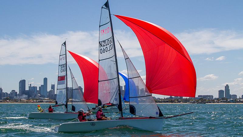 Two boats with red sails on the water in front of a skyline