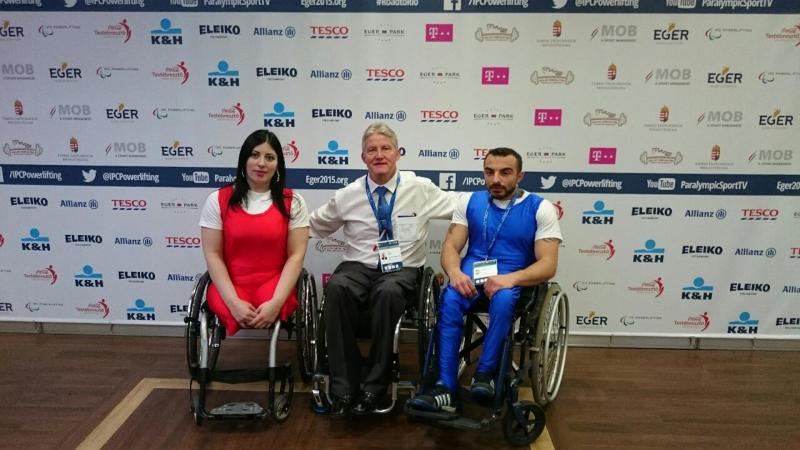 Two athletes posing with a man in front of a branded backdrop