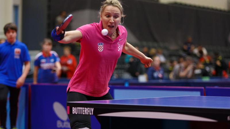 the upper body of a female playing table tennis and wearing a pink polo shirt