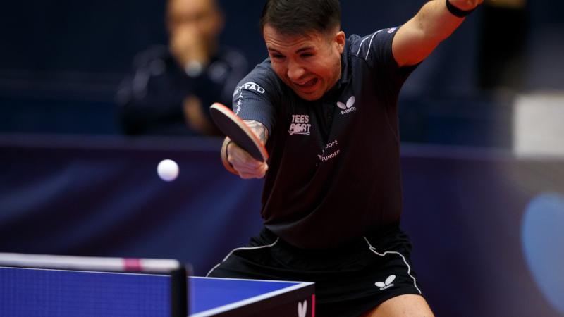 A man wearing a navy shirt playing table tennis