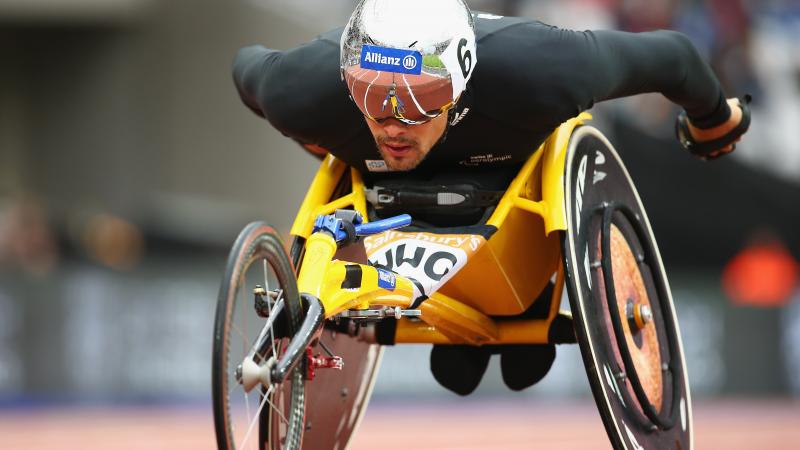 a male wearing black and a helmet racing in a wheelchair