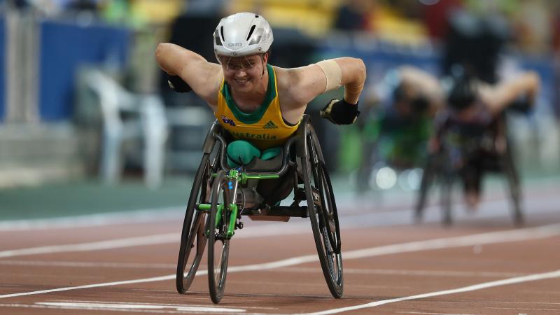 a female from Australia competing in a wheelchair with green and yellow clothes and a white helmet