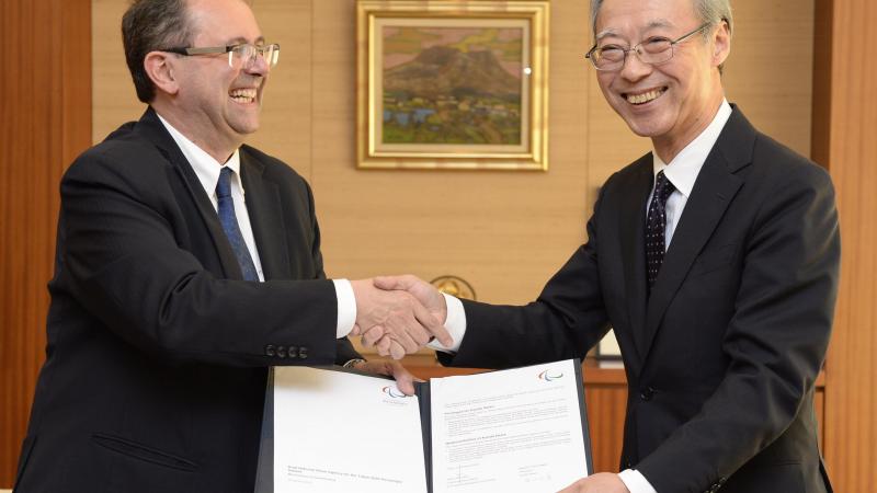 Two men shaking hands, holding a document