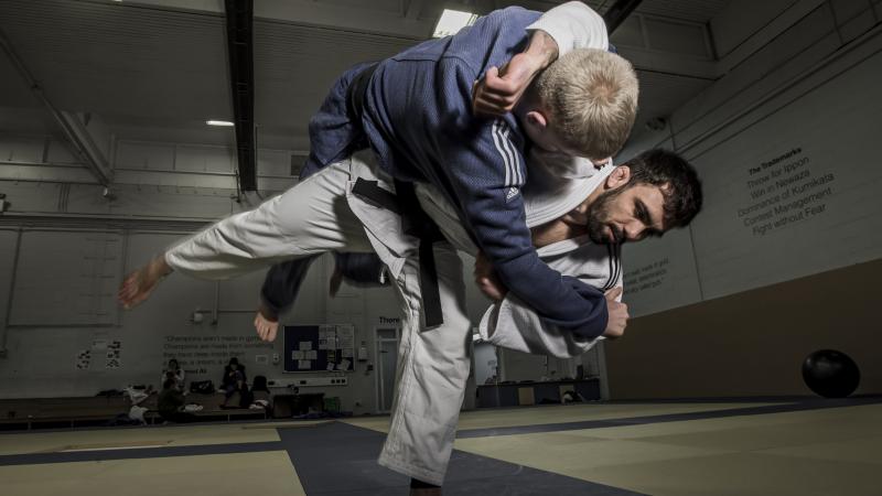 A male judoka in a while suit puts a move on another male judoka in a blue suit. 