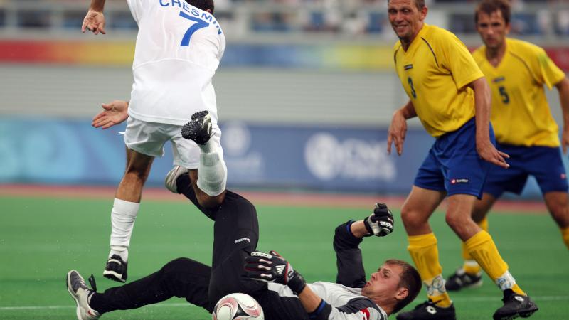 Man on the ground. other man jumping over him. Both focusing on a ball