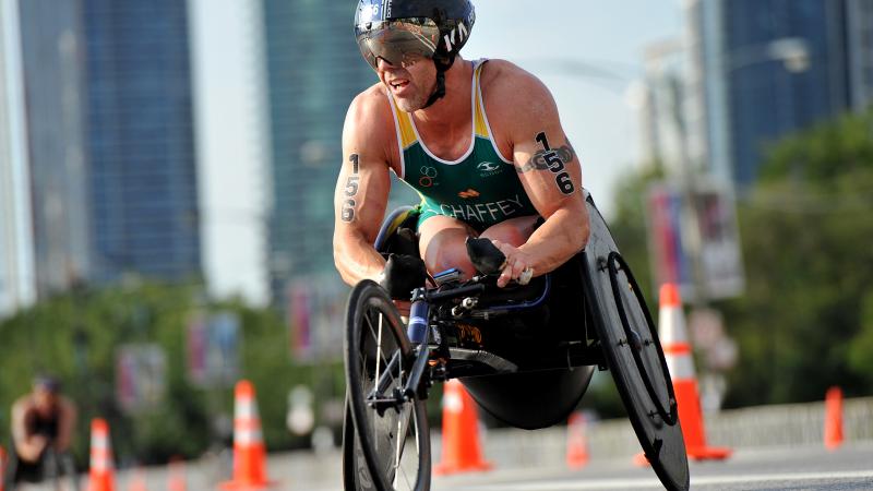 Man in green jersey in a racing wheelchair on a street