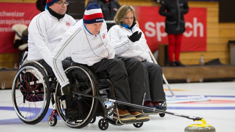 Wheelchair curler on the ice with team in the background