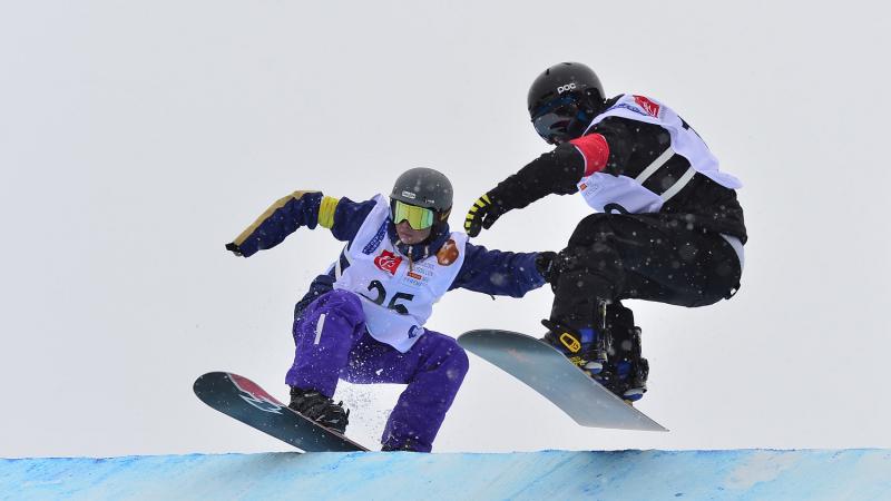 Two snowboarders jumping during a run