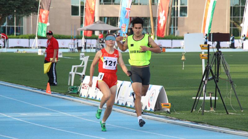 A visually impaired runner runs with her guide