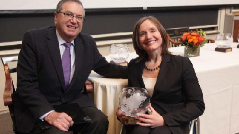 Woman in wheelchair holds trophy and poses with man.