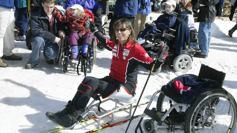 Woman in sit-ski speaks to children. 