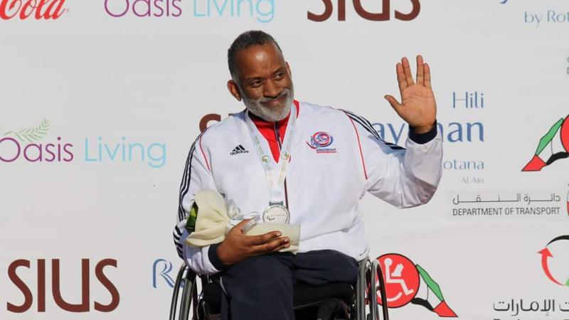 Man in wheelchair holding a medal, waving