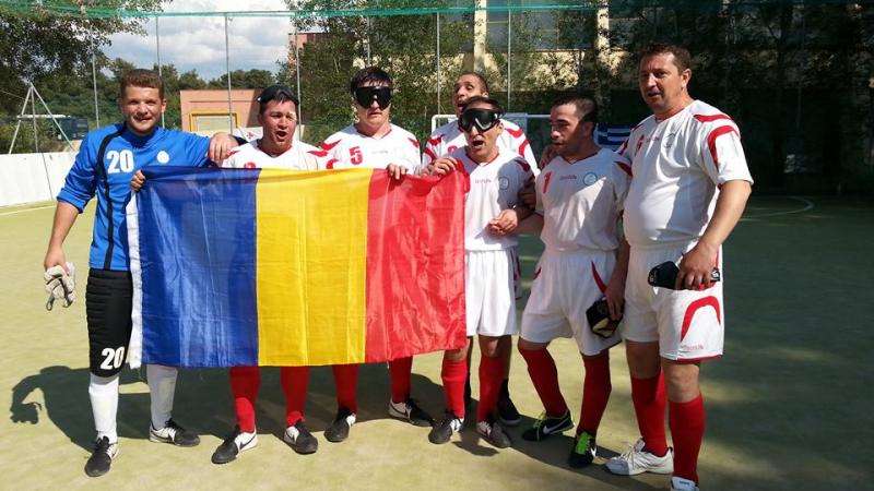 Seven men, some of them blindfolded hold a Romanian flag, celebrate.