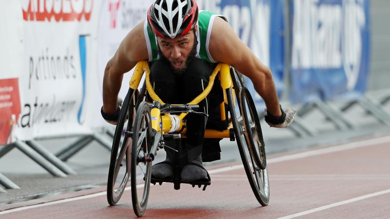 A man in a yellow racing chair pushes forward in the outside lane of a race.